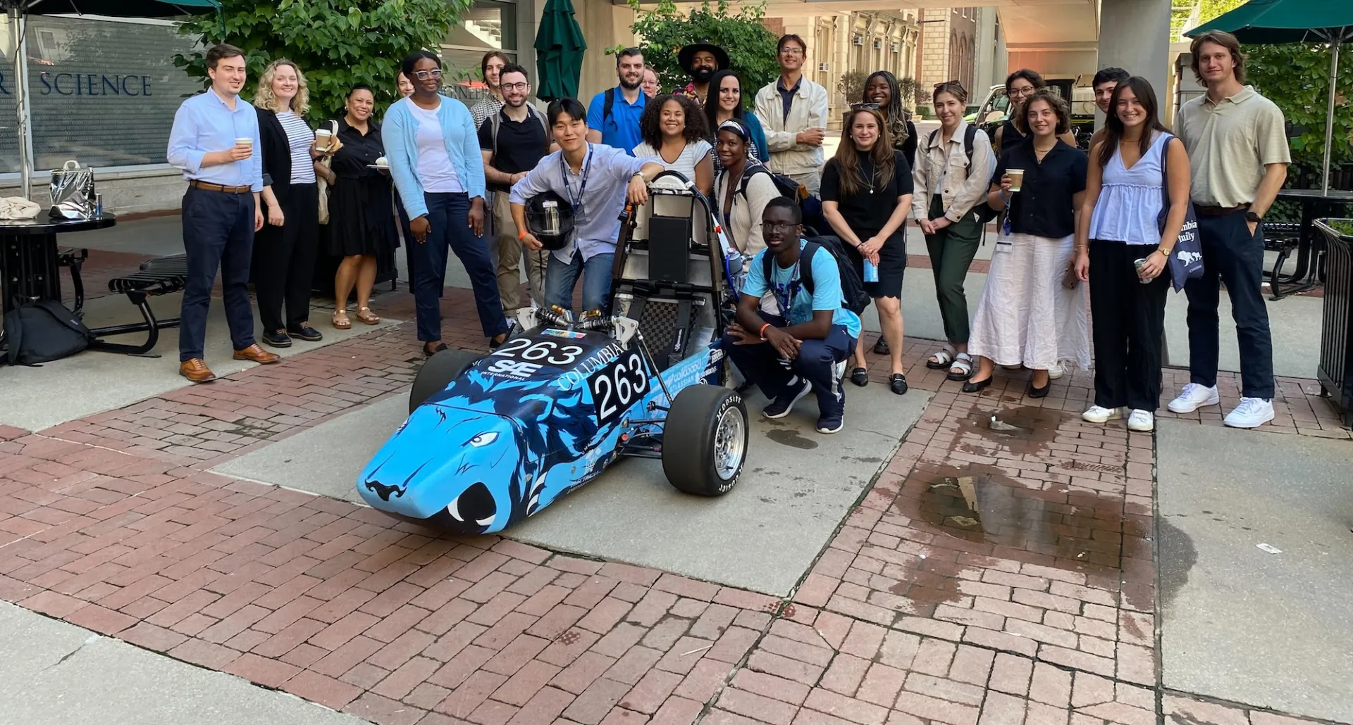 Columbia Engineering staff and Formula Racing team members posing for a photo with their race car outside the Mudd building