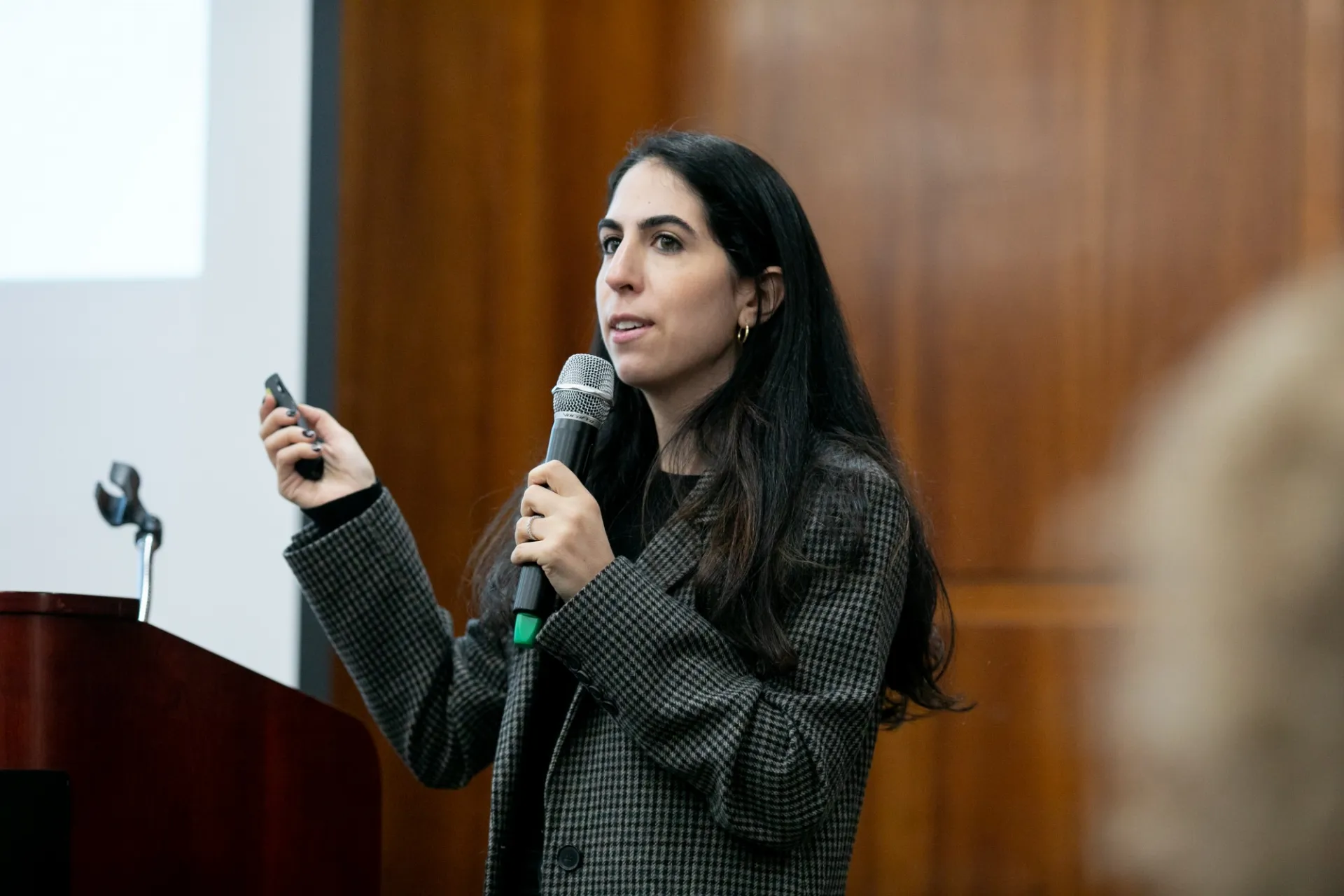 A speaker holding a microphone and clicker addresses an audience.