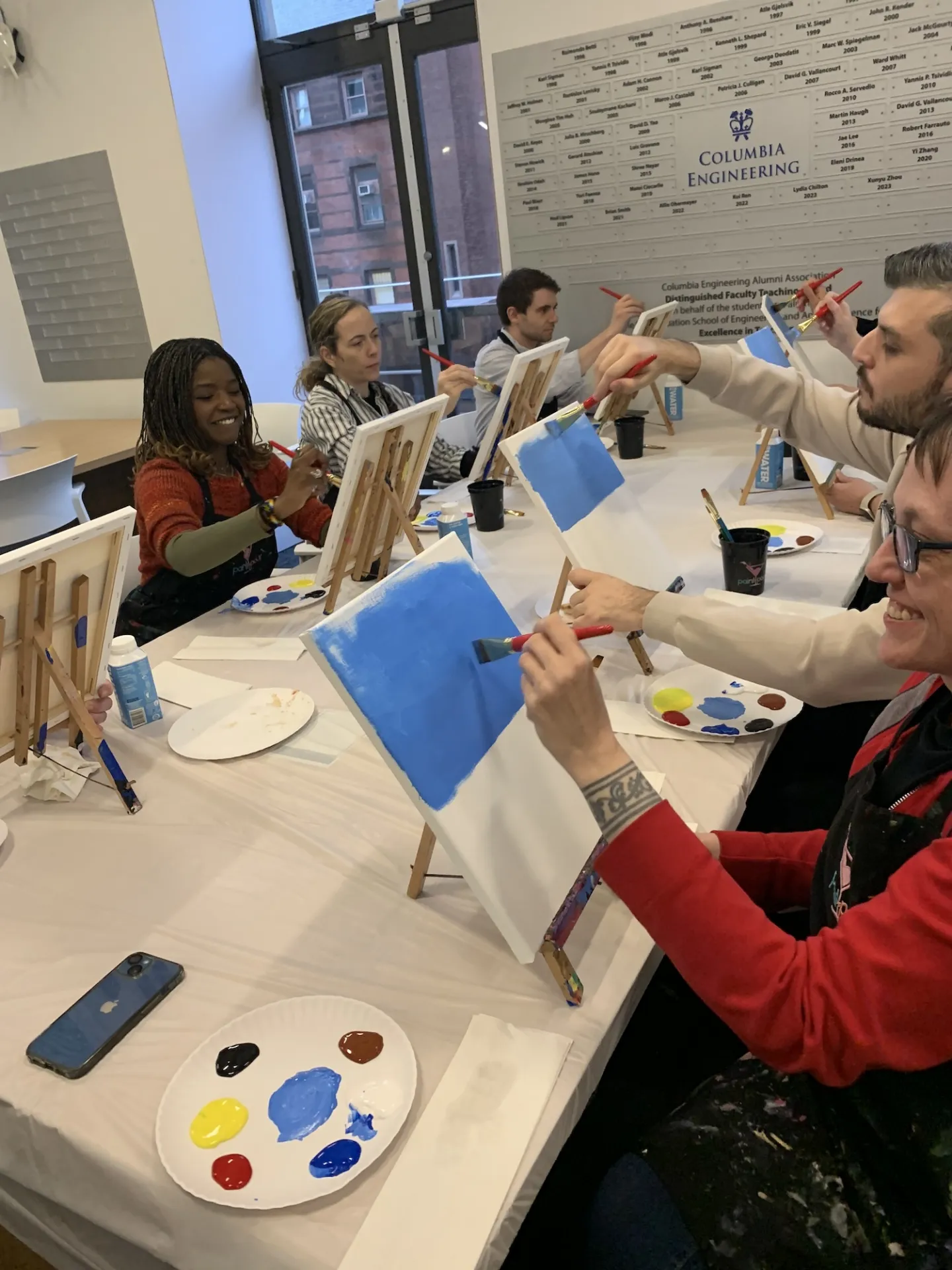 Columbia Engineering staff members sitting at a table and painting backgrounds into canvases