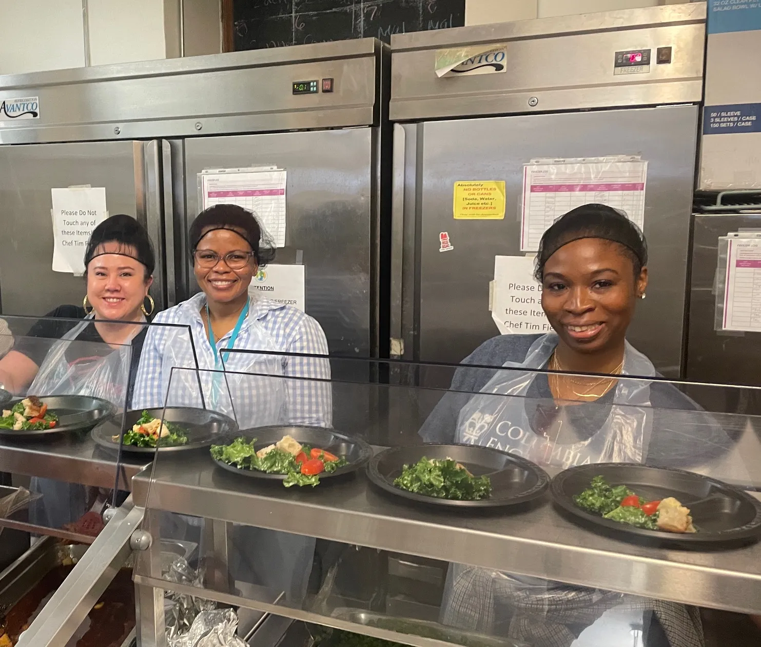 Three staff smiling while preparing meals 