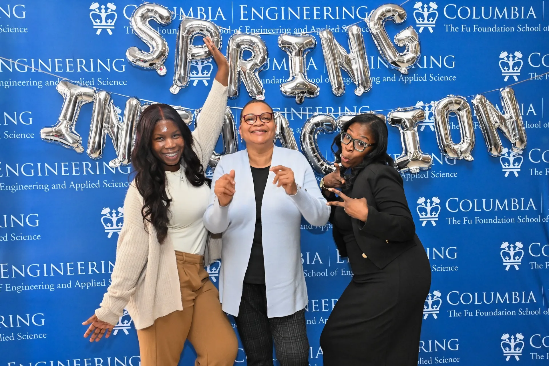 Three Columbia staff posing in front of balloons that read "Spring into Action"
