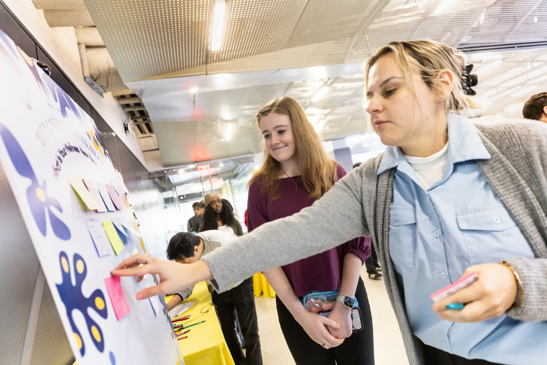 Two staff adding a sticky note to a poster board