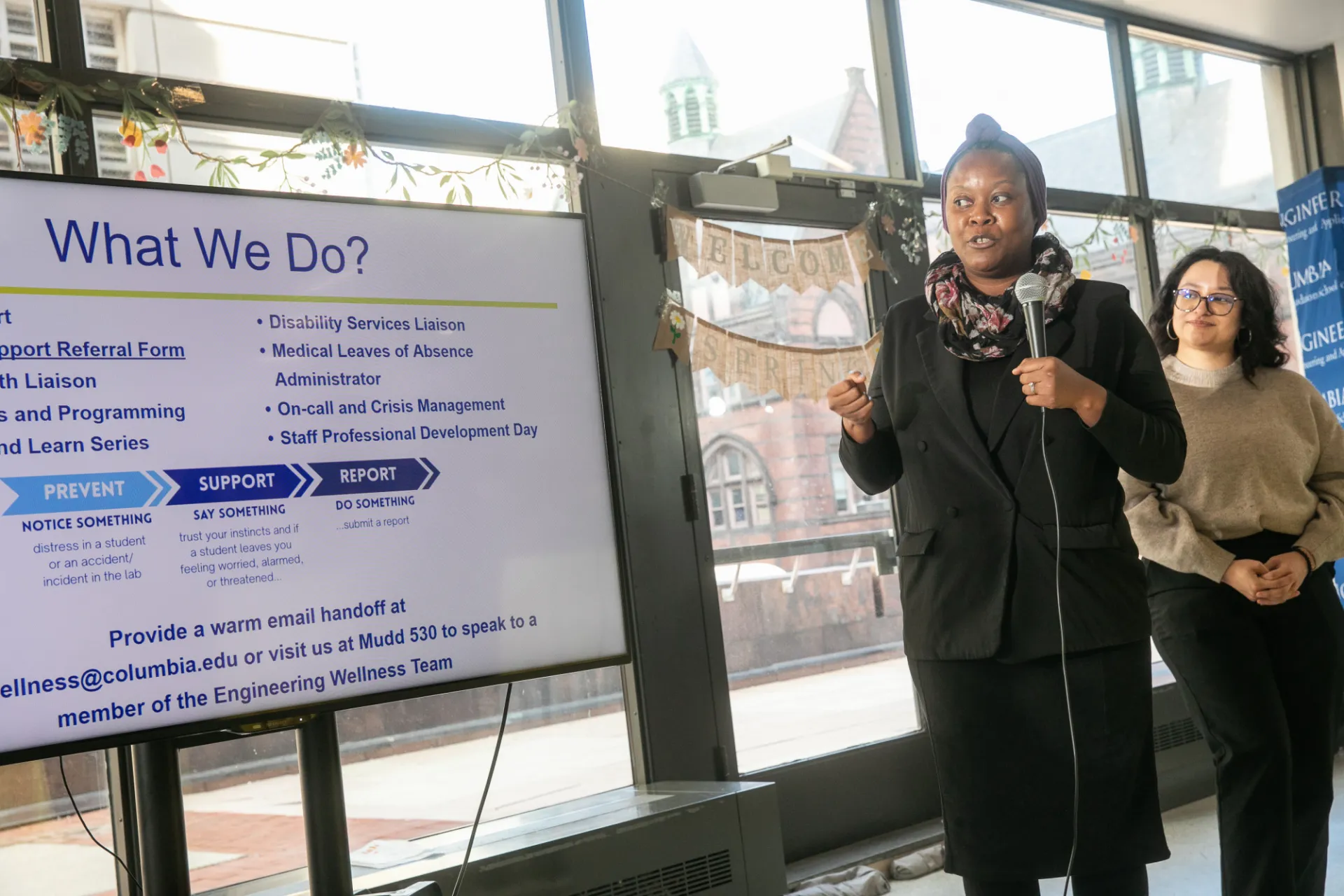 Another leader with her team member behind her giving a presentation titled What We Do?