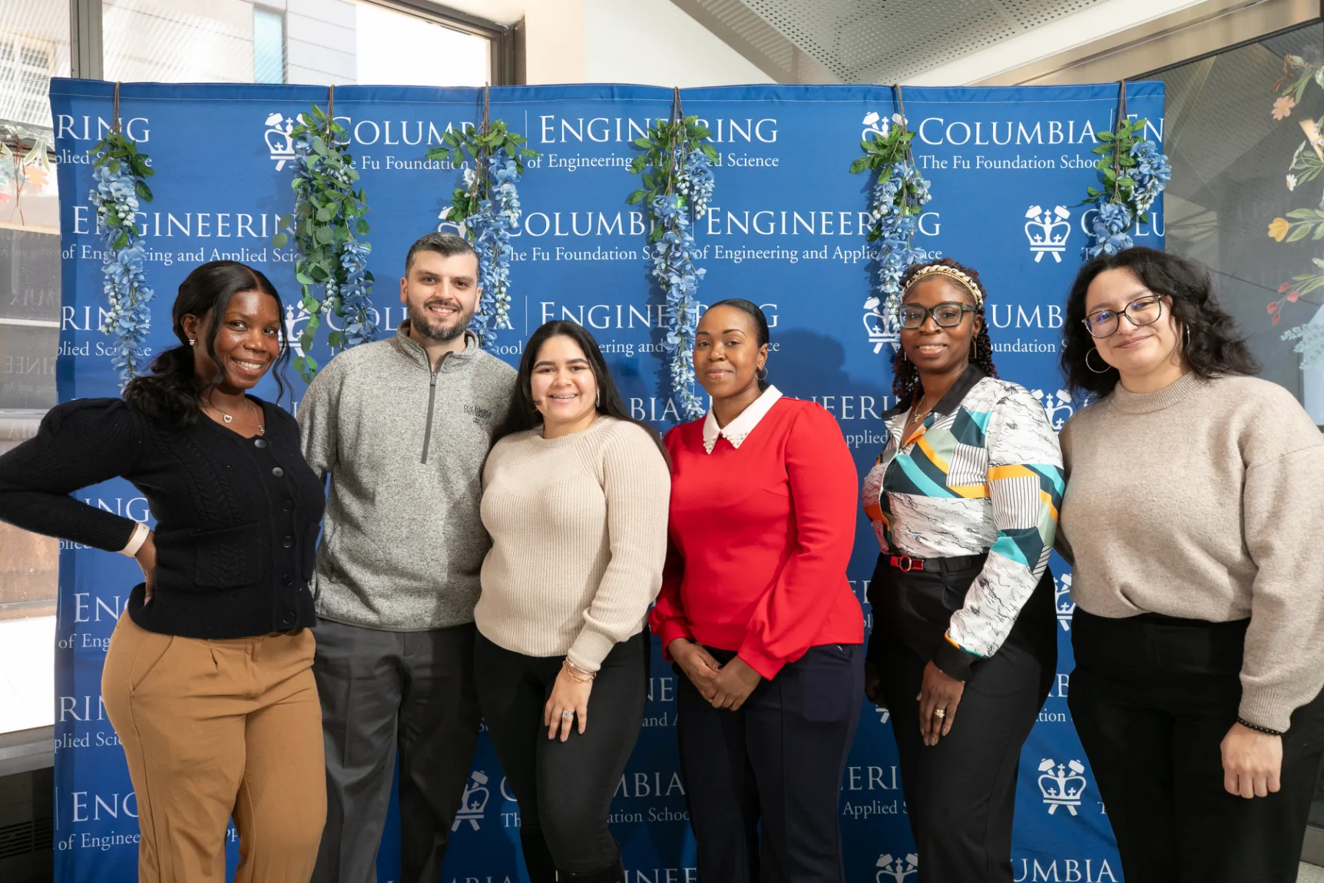 Six SEAS staff posing in front of a banner with flowers