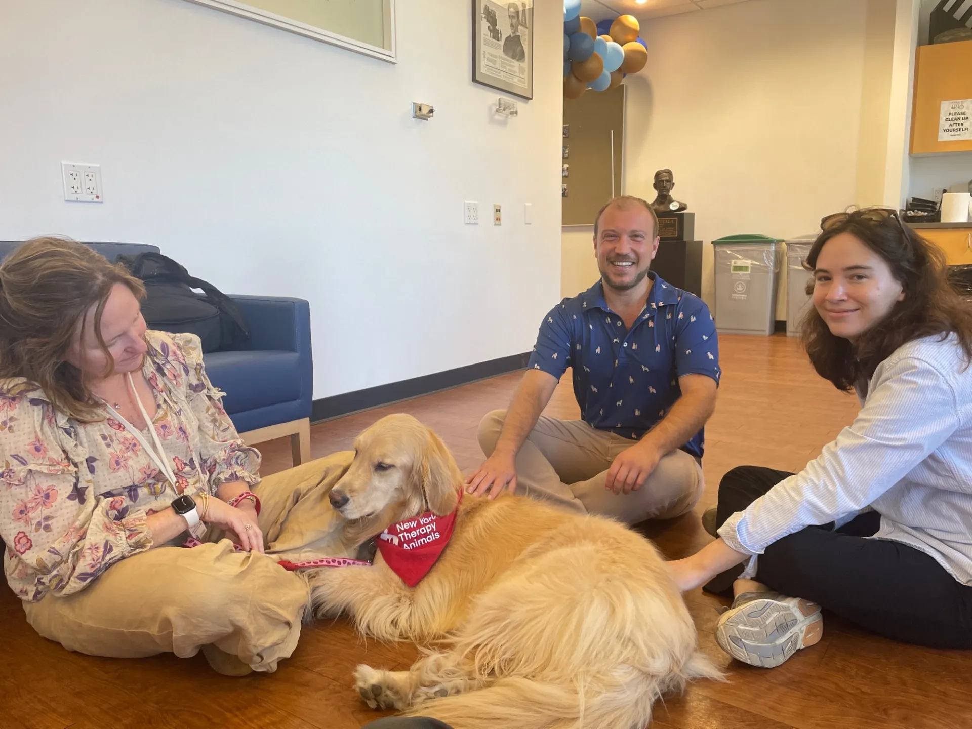 Three people smiling while petting a golden retriever 