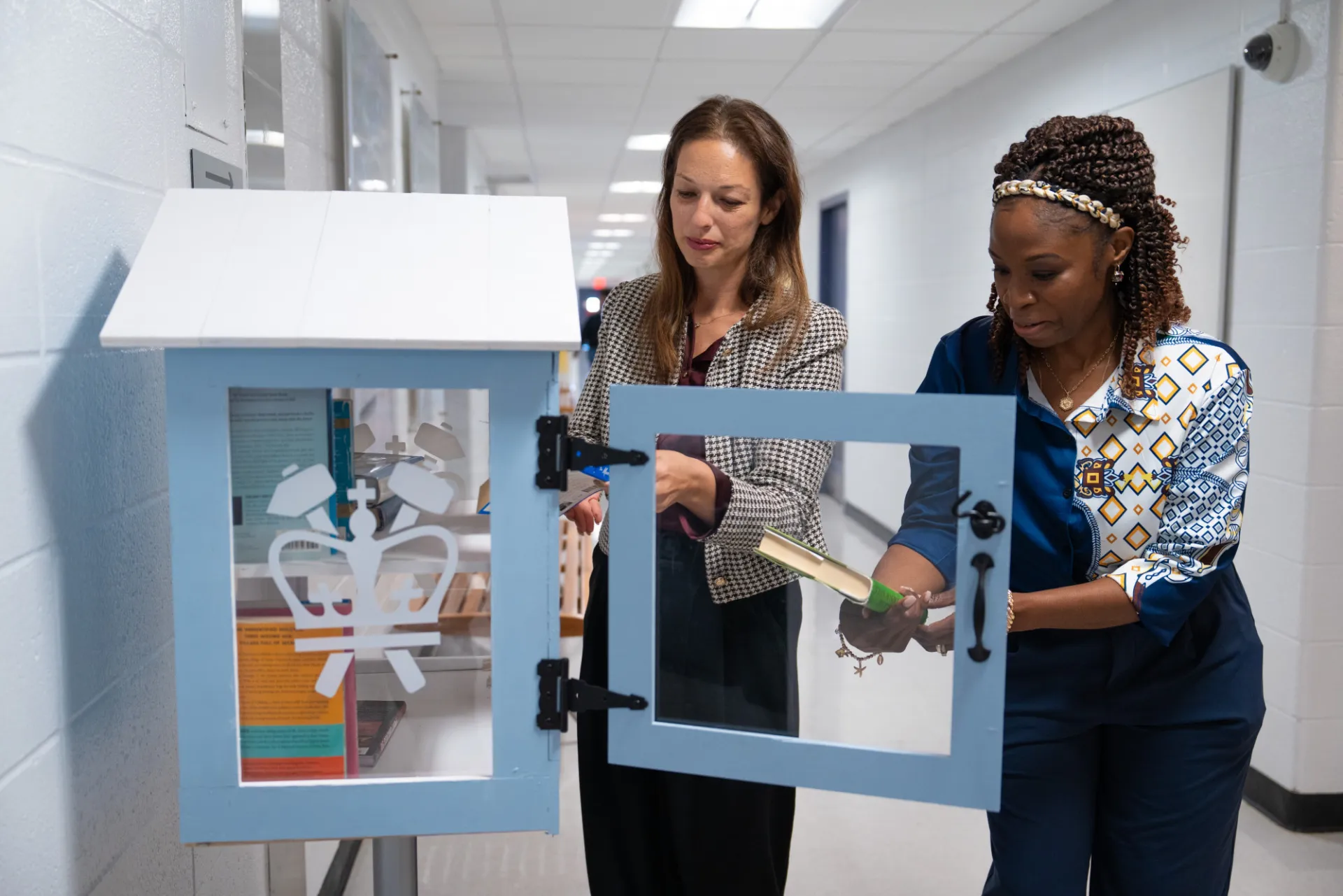 Two staff members looking at some books inside little library